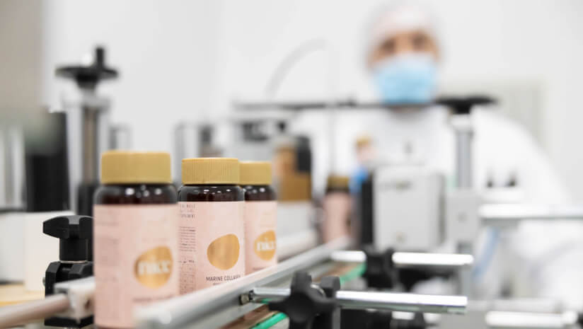 Person overseeing the production and bottling of dietary supplements in a factory setting.