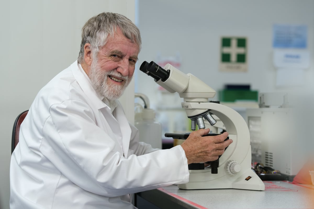 Professor Emeritus John Tagg is the founder of BLIS Technologies sitting at a microscope