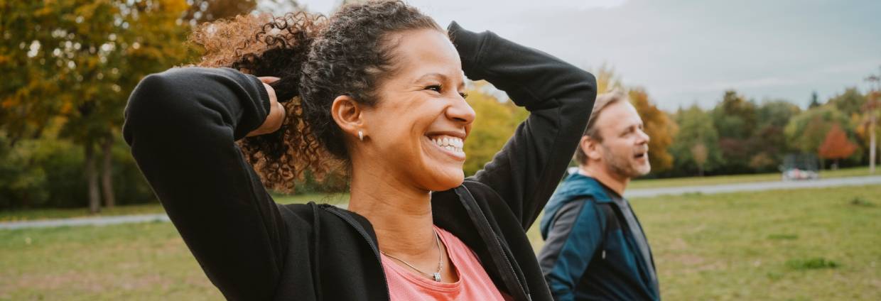 Cheerful woman tying hair by male friend in park