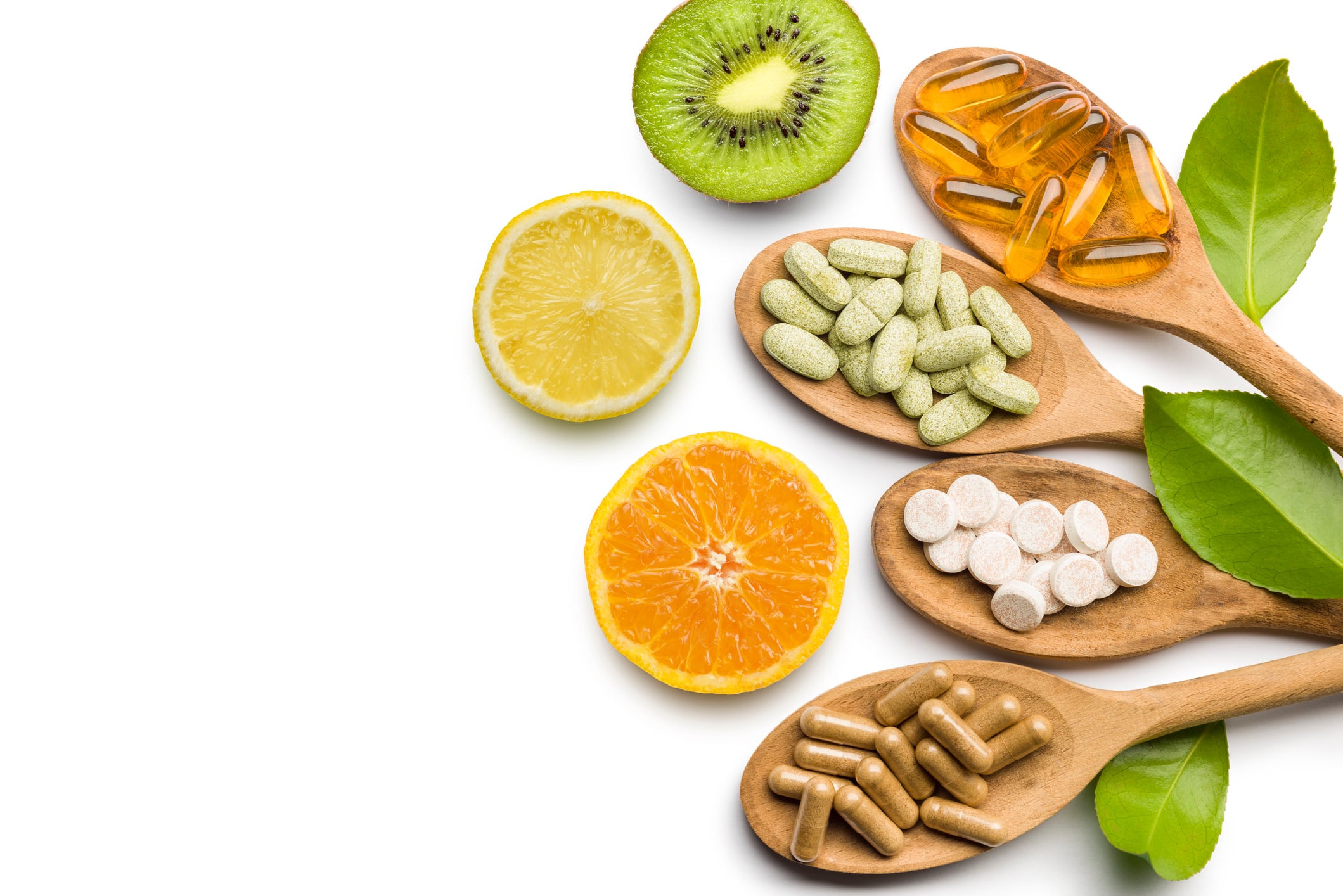 Supplement pills on wooden scoop with citrus fruits on white background