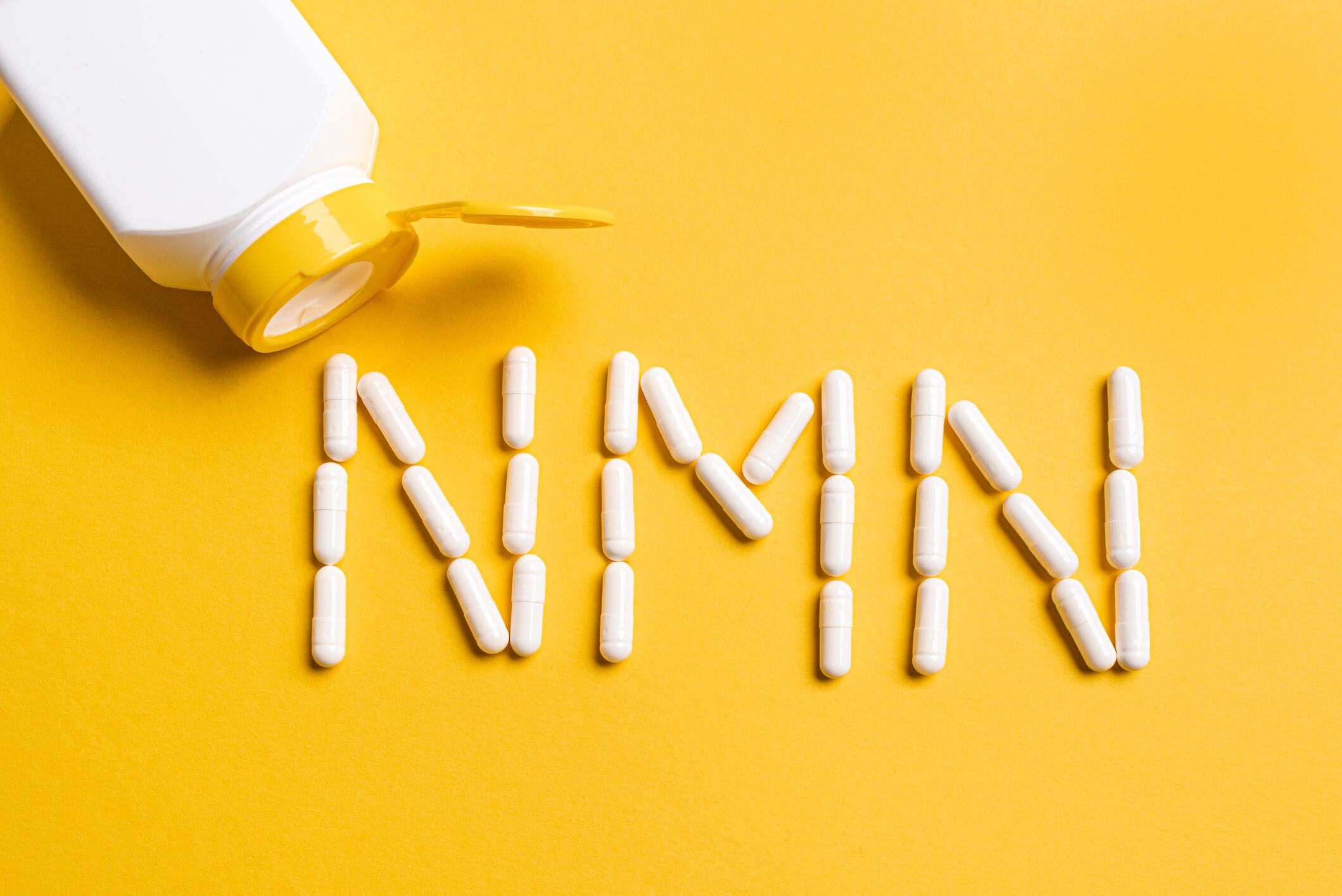 Nicotinamide mononucleotide supplement, niacin, anti ageing vitamin. White pills forming shape to NMN letters on yellow background, copy space, top view.