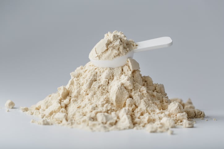 A mountain of  protein in powder with a measuring spoon on a white background.
