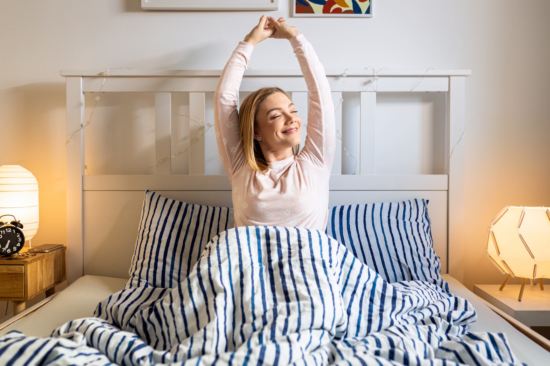 Woman awakens in a cozy bed and stretches in bedroom with soft morning light creating a peaceful atmosphere.