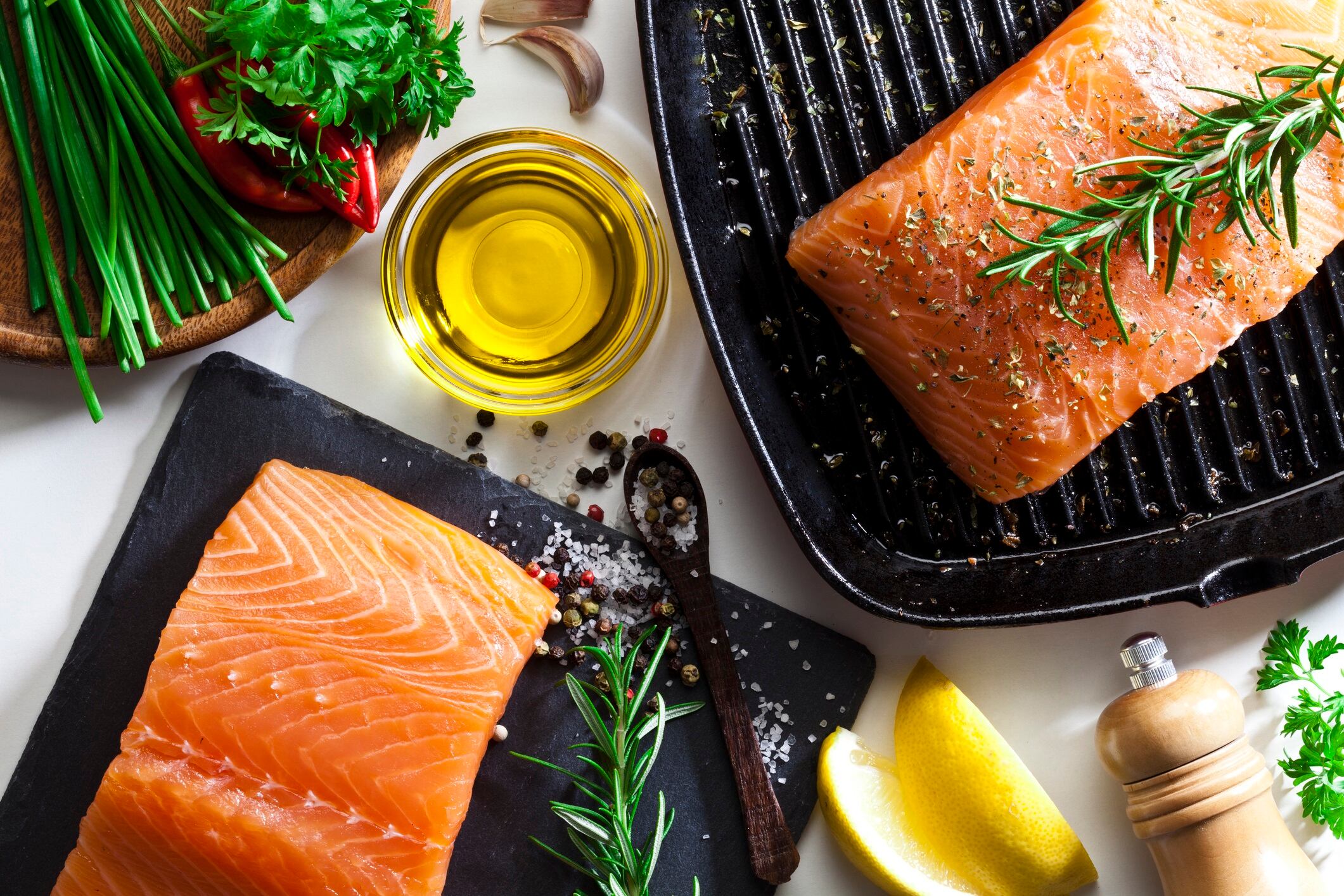 Top view of two raw salmon steaks ready for cooking. Some ingredients for cooking salmon like salt, pepper, rosemary, chive, lime and olive oil are all around the frame.
