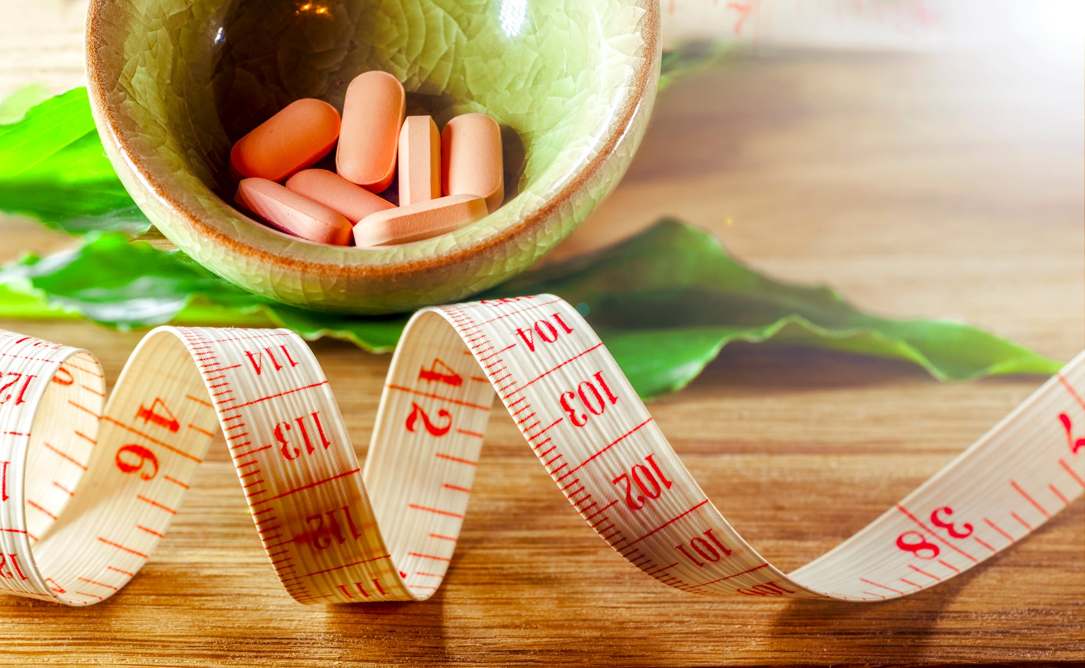 Dietary pills and tape measure on wooden background.